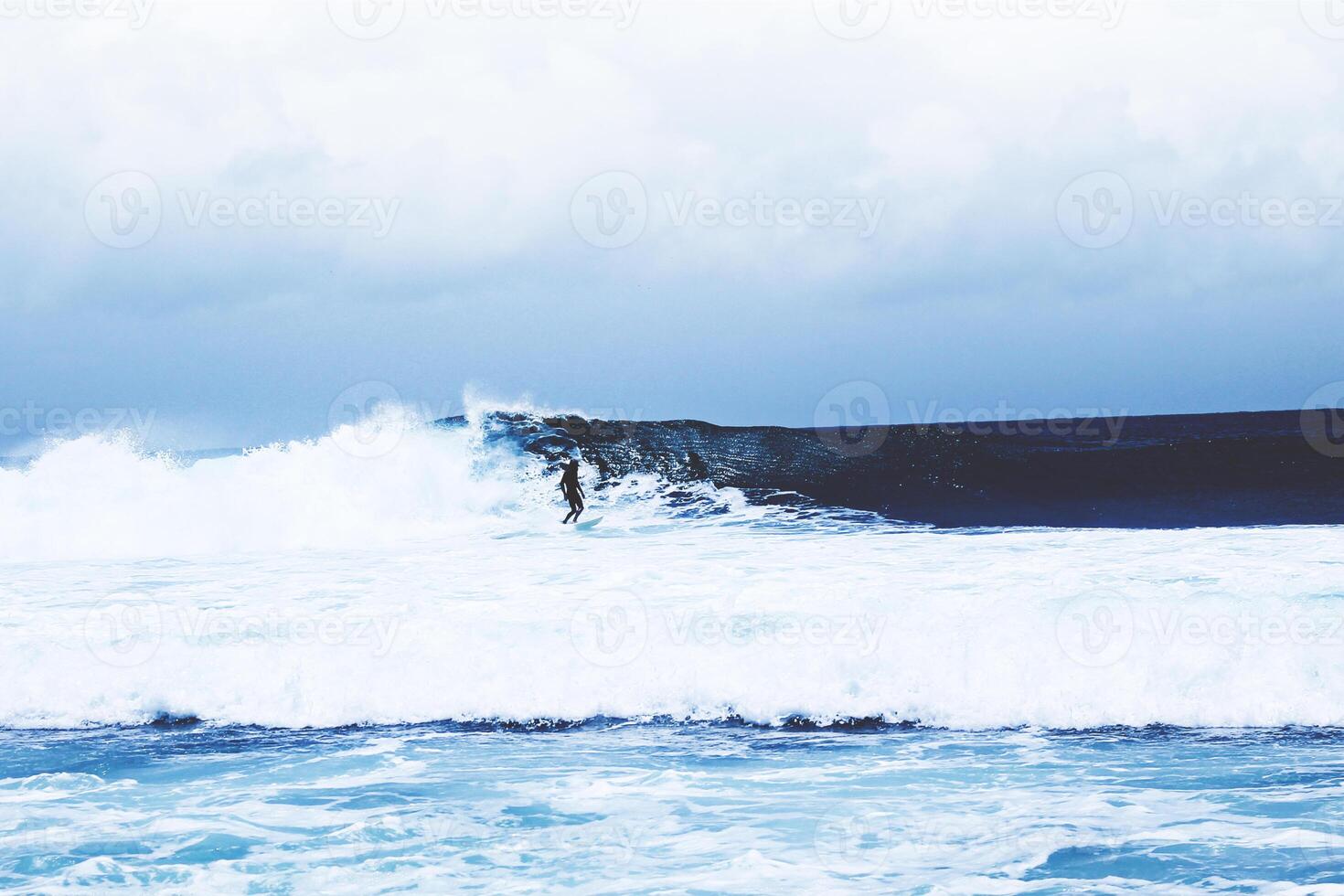 A distant surfer riding a rough ocean wave photo