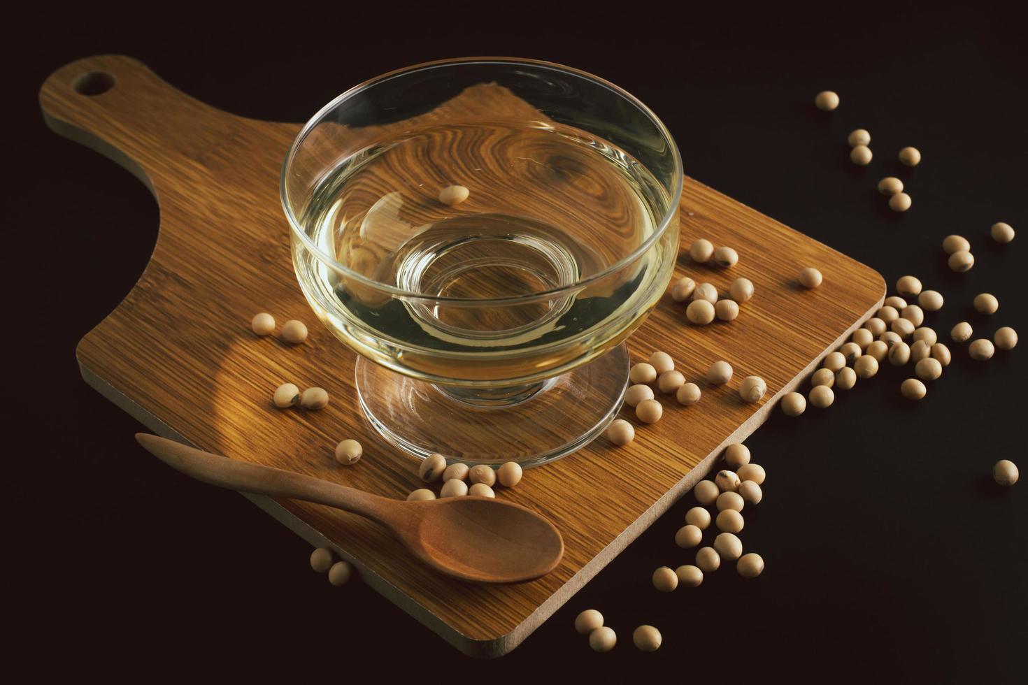 soybean and bowl with oil on a wooden cutting board on black background, front view,selective focus. photo