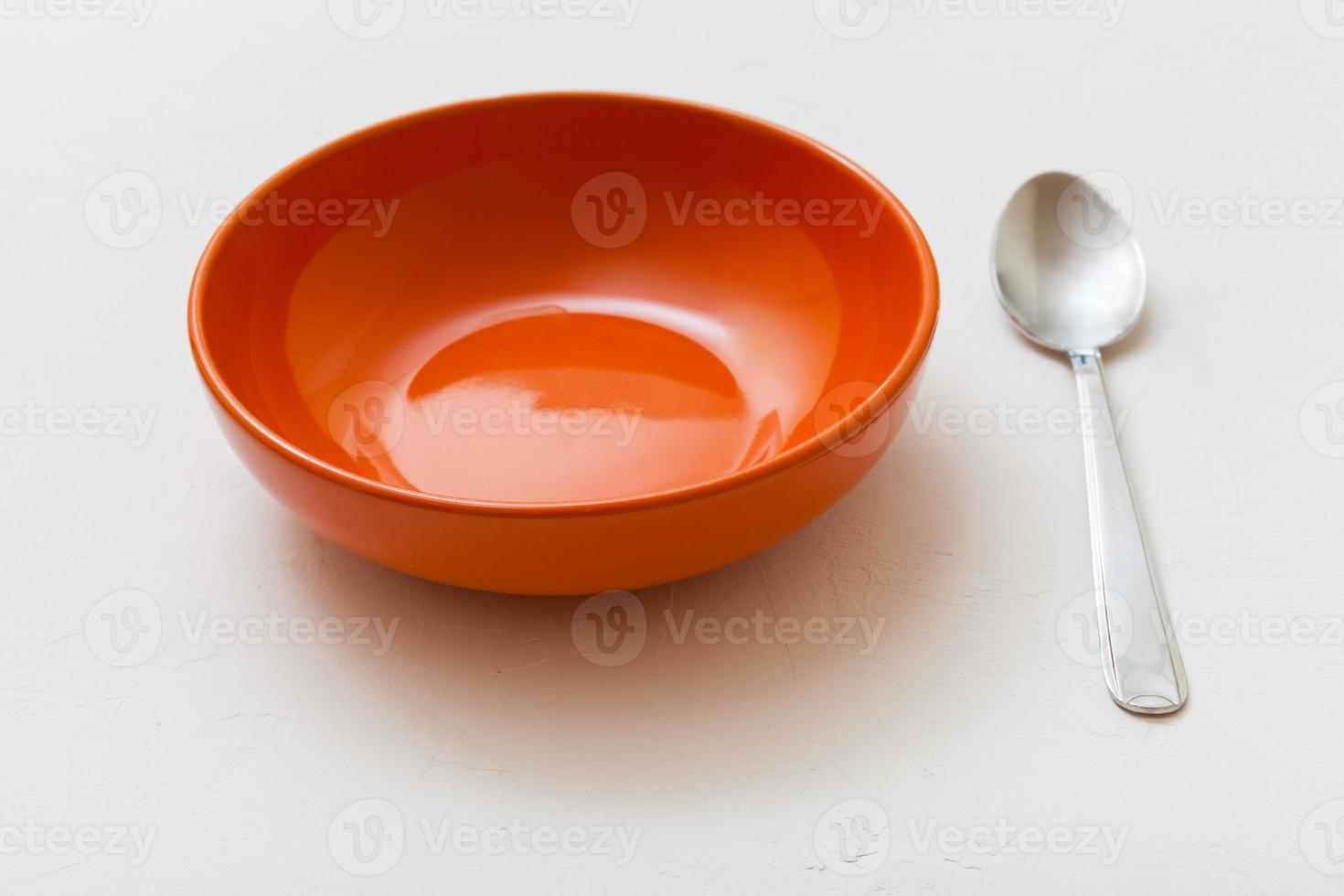 orange bowl and spoon on white plaster photo