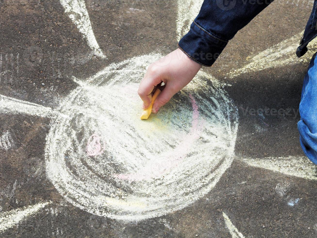 girl paints a sun with colored chalk on asphalt photo