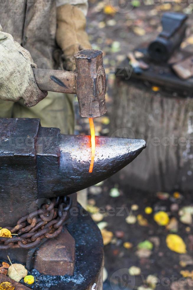 Blacksmith forges red glowing iron rod on anvil photo