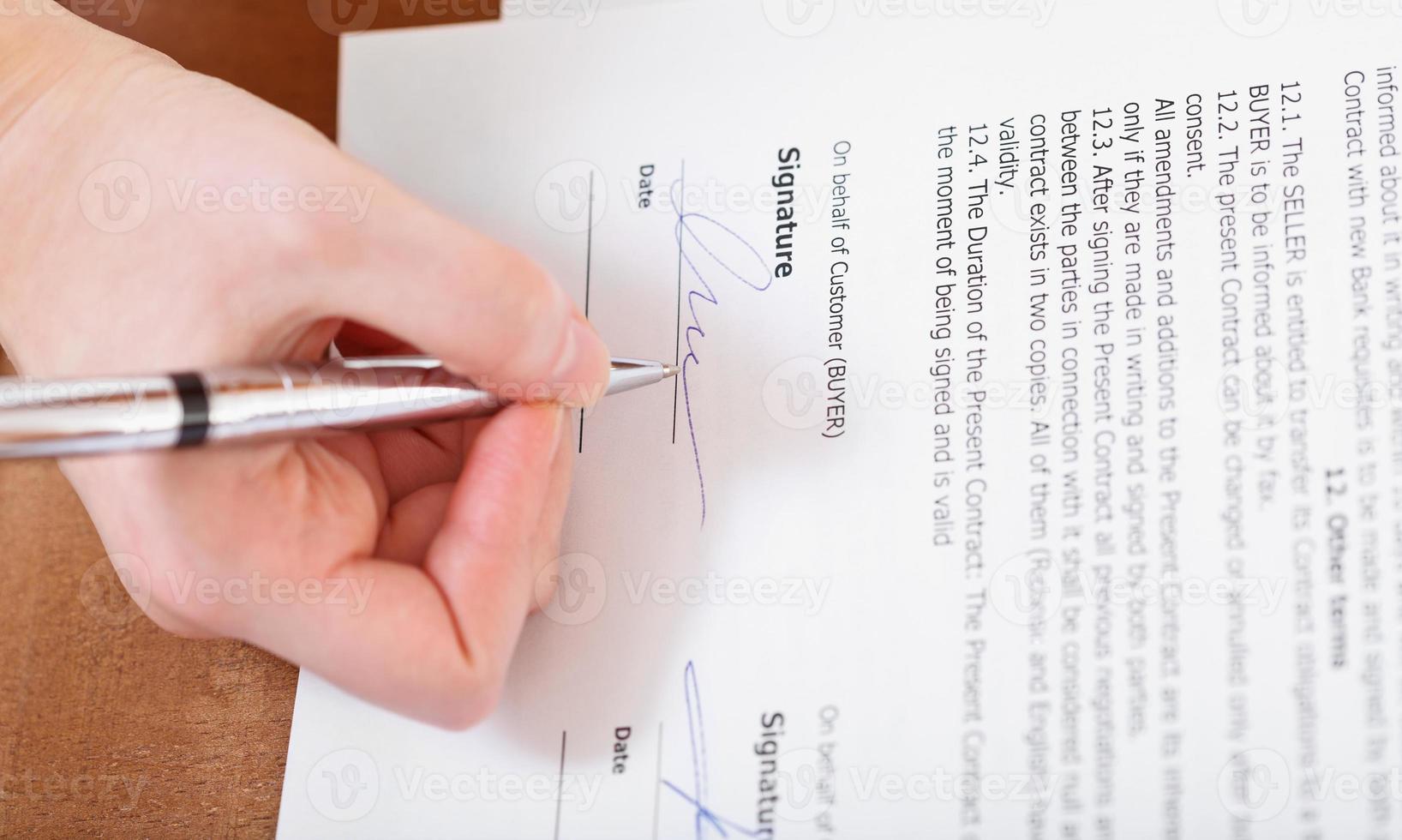 el comprador firma un contrato con un bolígrafo plateado foto