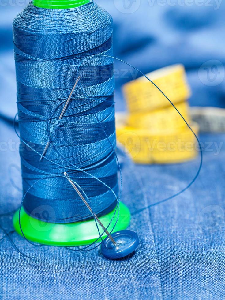 thread bobbin, button, measure tape on blue fabric photo