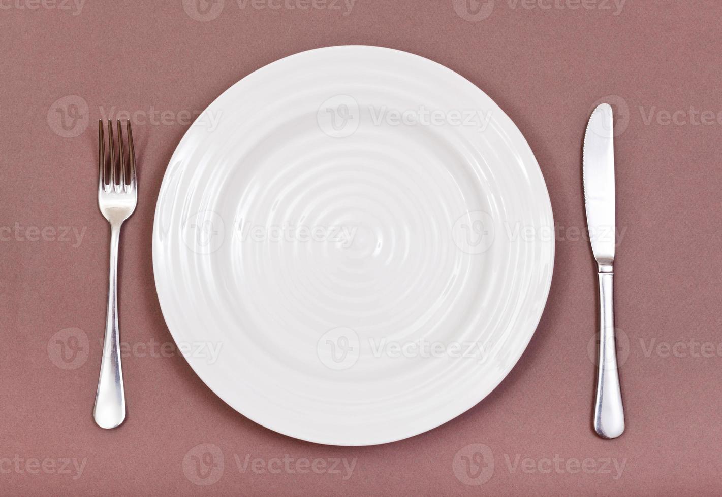 top view of white plate, fork, knife set on brown photo