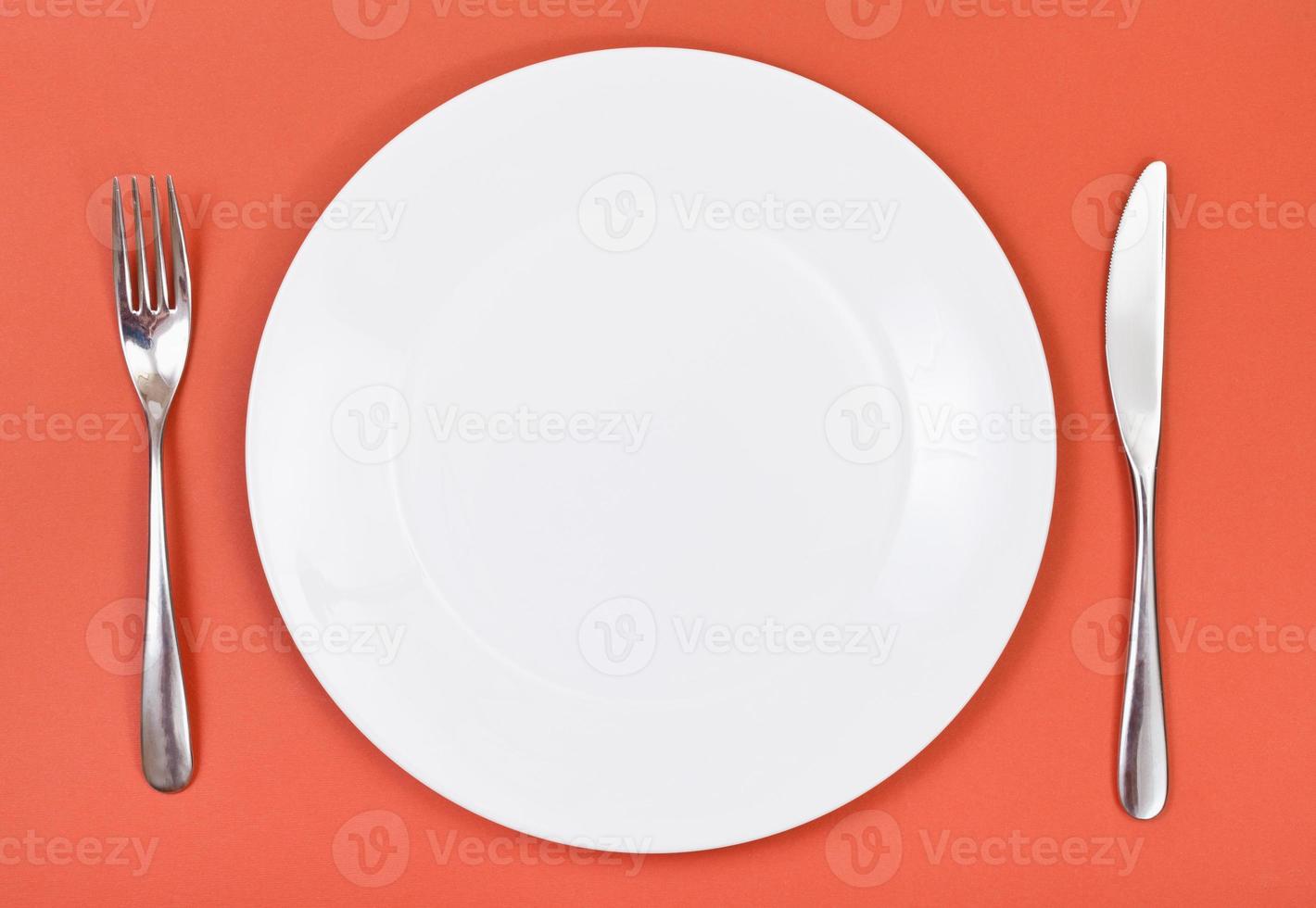 top view of porcelain plate, fork, knife on red photo