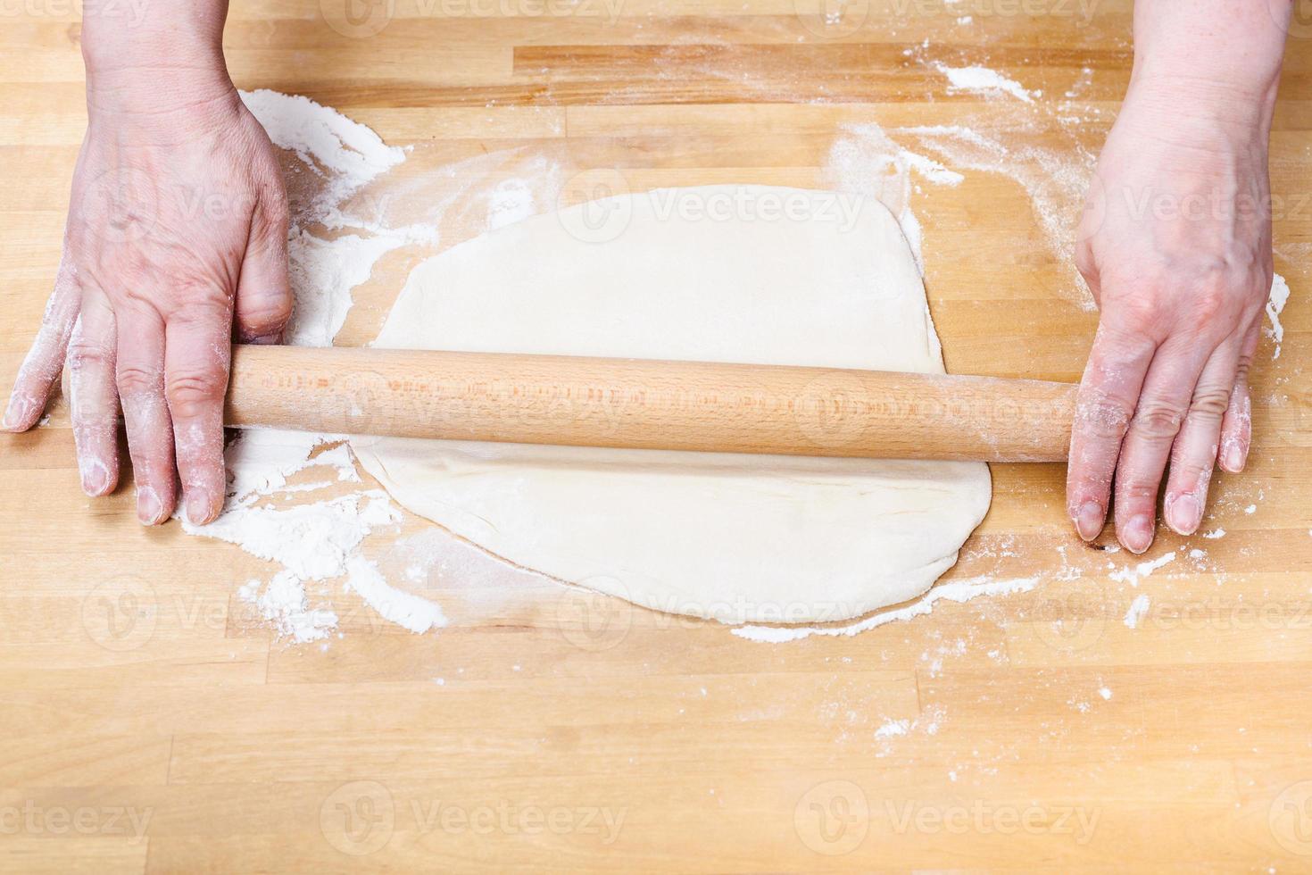 female hands roll out dough with rolling pin photo