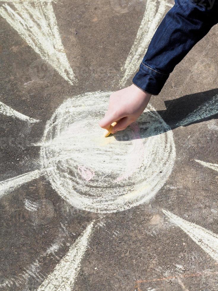 girl drawing a sun with colored chalk on pavement photo