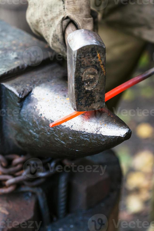 herrero forja varilla de acero al rojo vivo en el yunque foto
