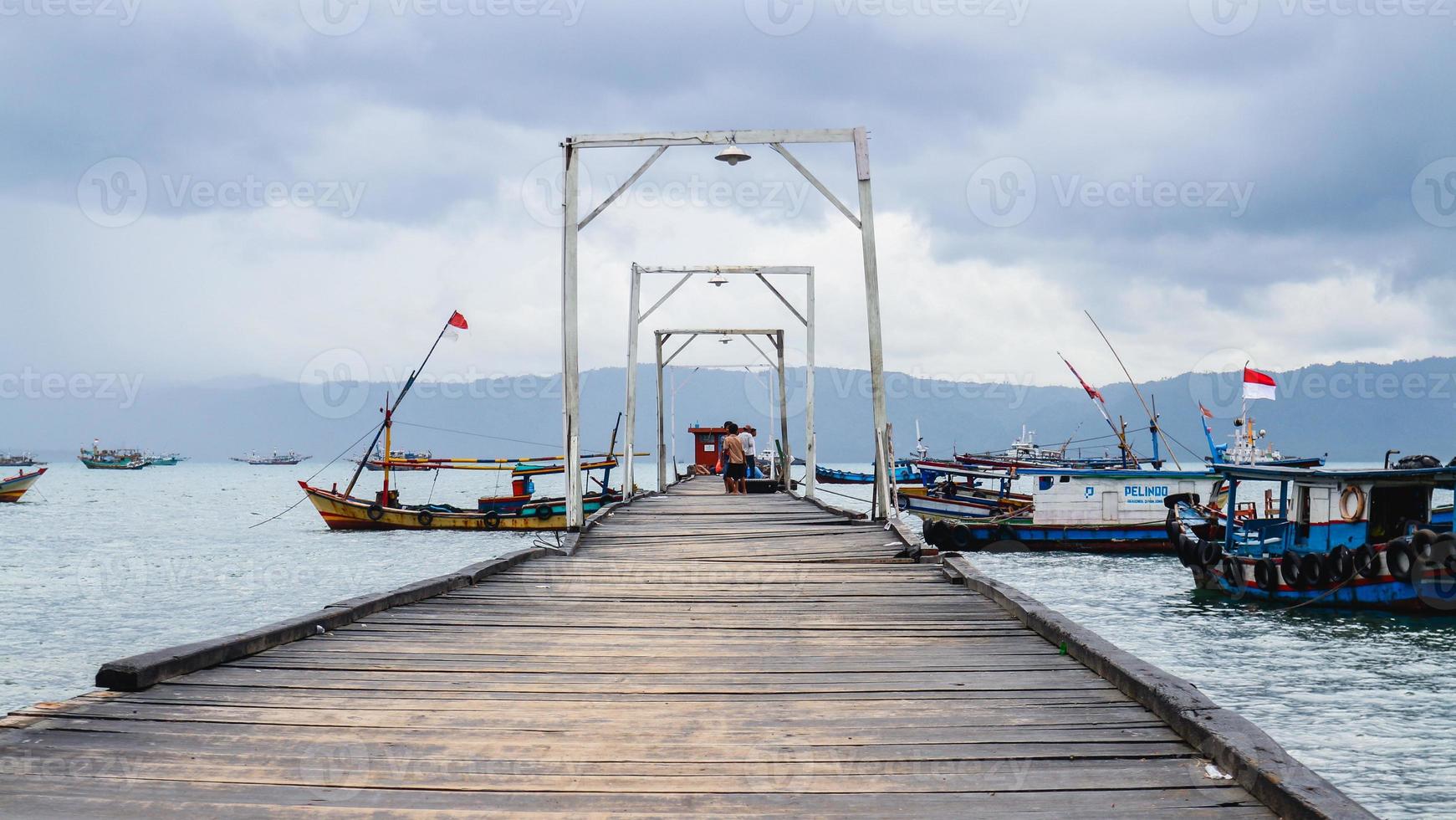Wood bridge leading to the middle of the sea where a fishermans boat lean on. Road to the middle of the sea photo