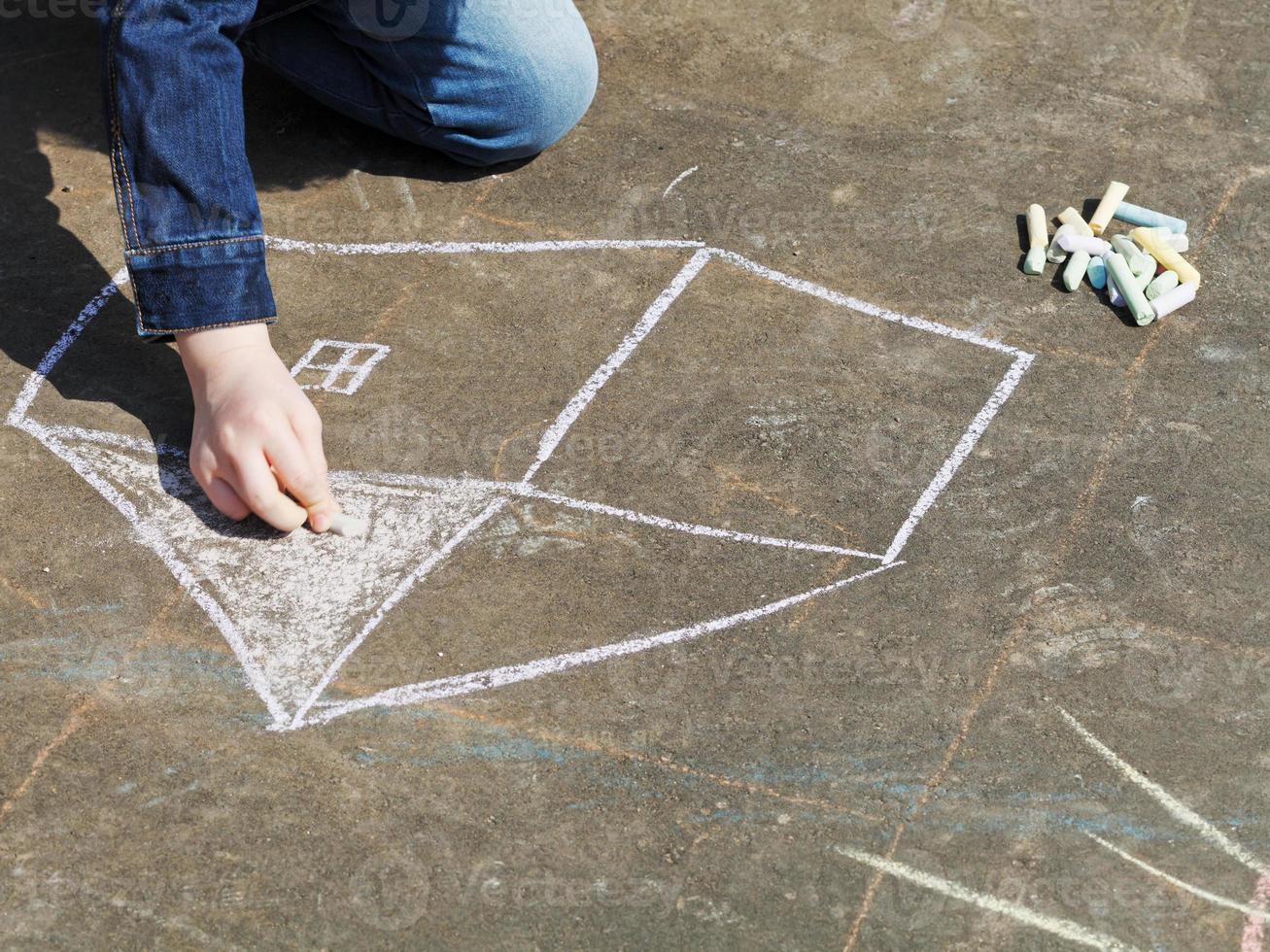 girl drawing house with colored chalk on pavement photo