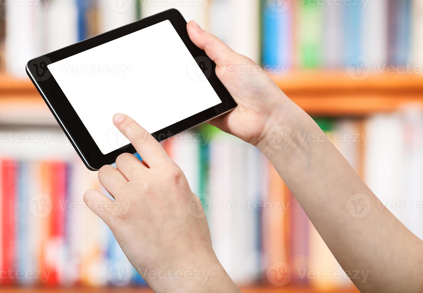 finger touches tablet pc on front of book shelves photo