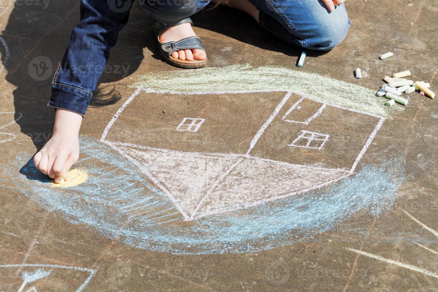 girl drawing a house with crayons on pavement photo