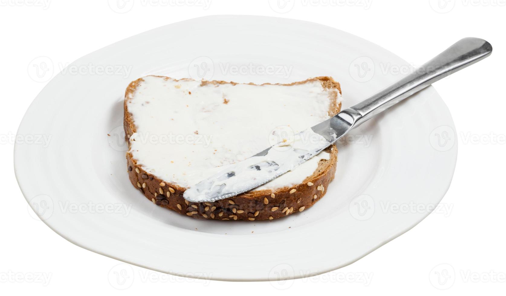 pan de grano con queso para untar y cuchillo en el plato foto