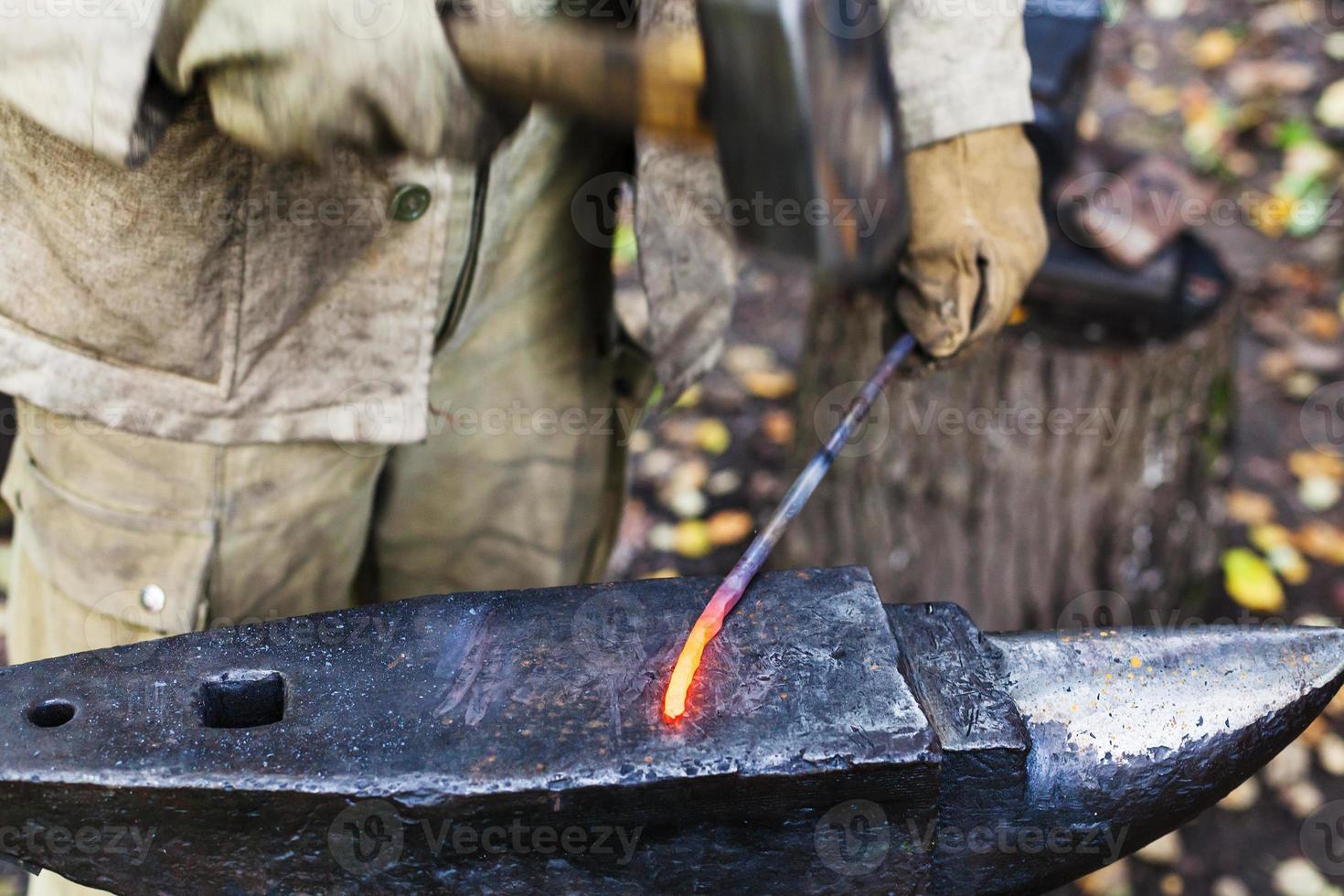 Blacksmith hammering red hot iron rod on anvil photo