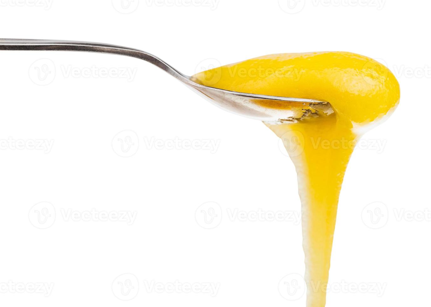 yellow dense honey flows down from metal spoon photo