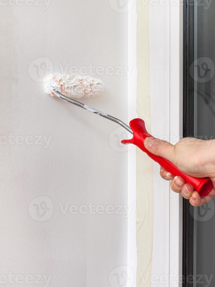 Worker paints window jamb with paint roller photo