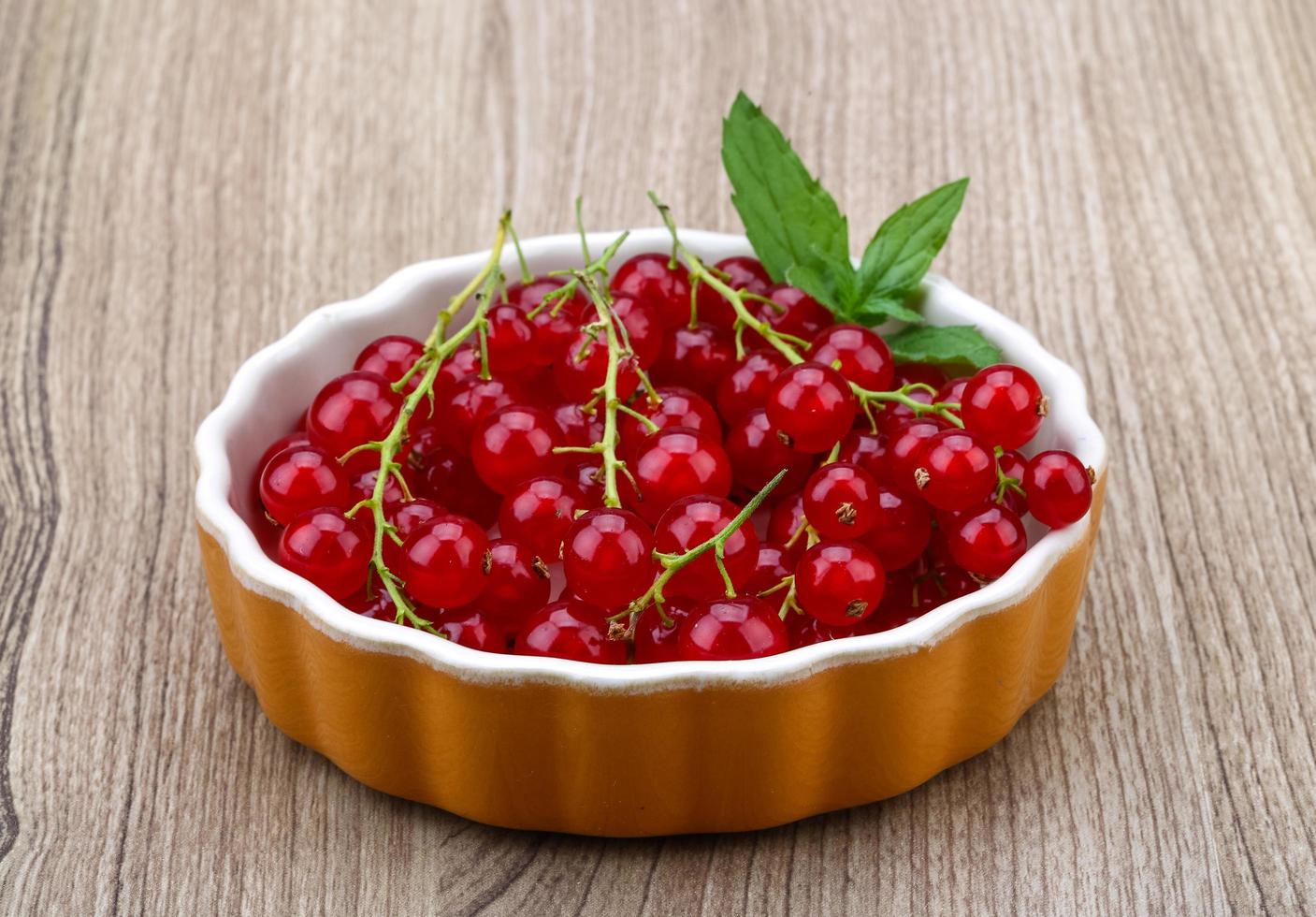 Red currant in a bowl on wooden background photo