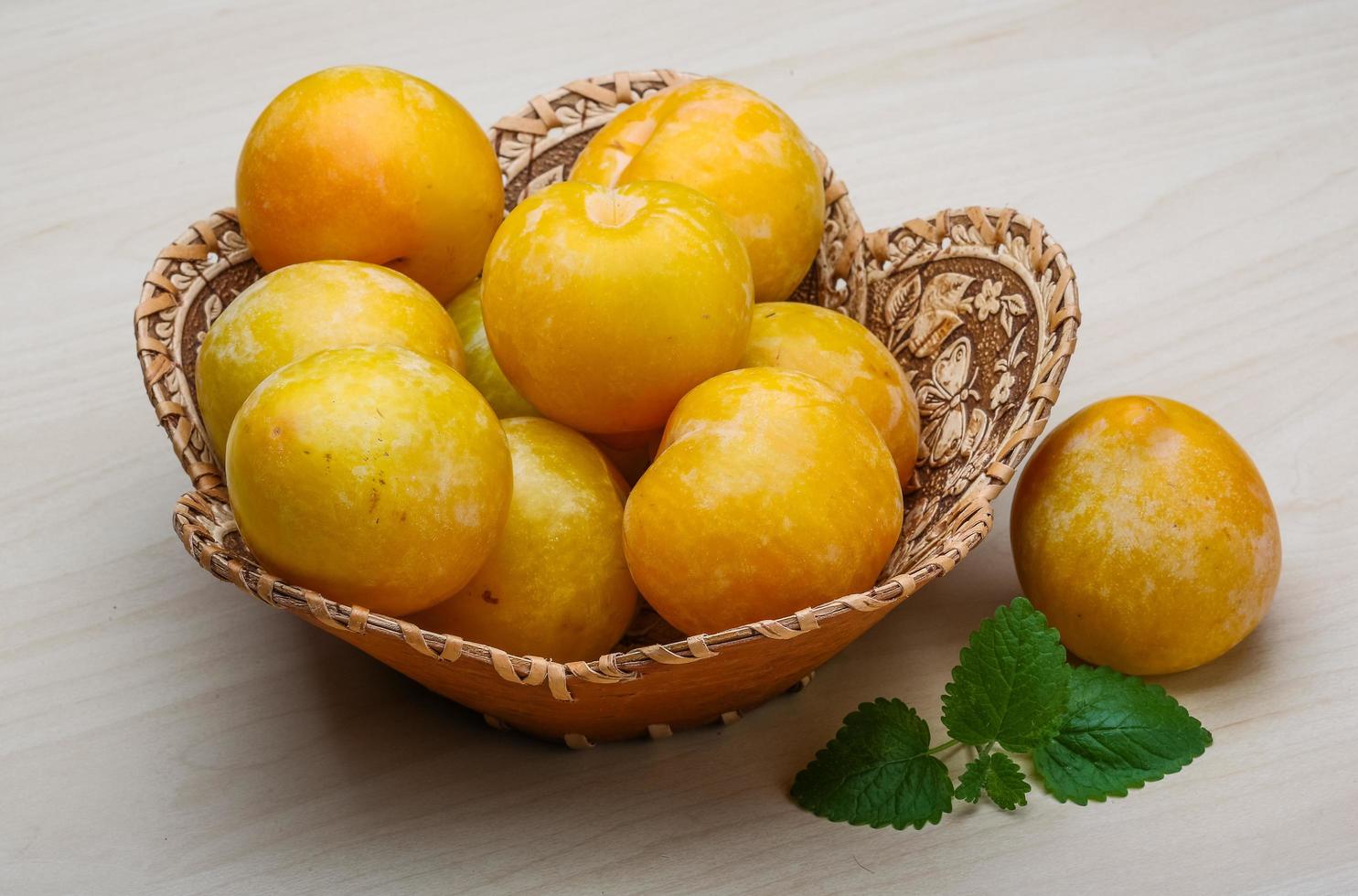 Yellow plums in a basket on wooden background photo