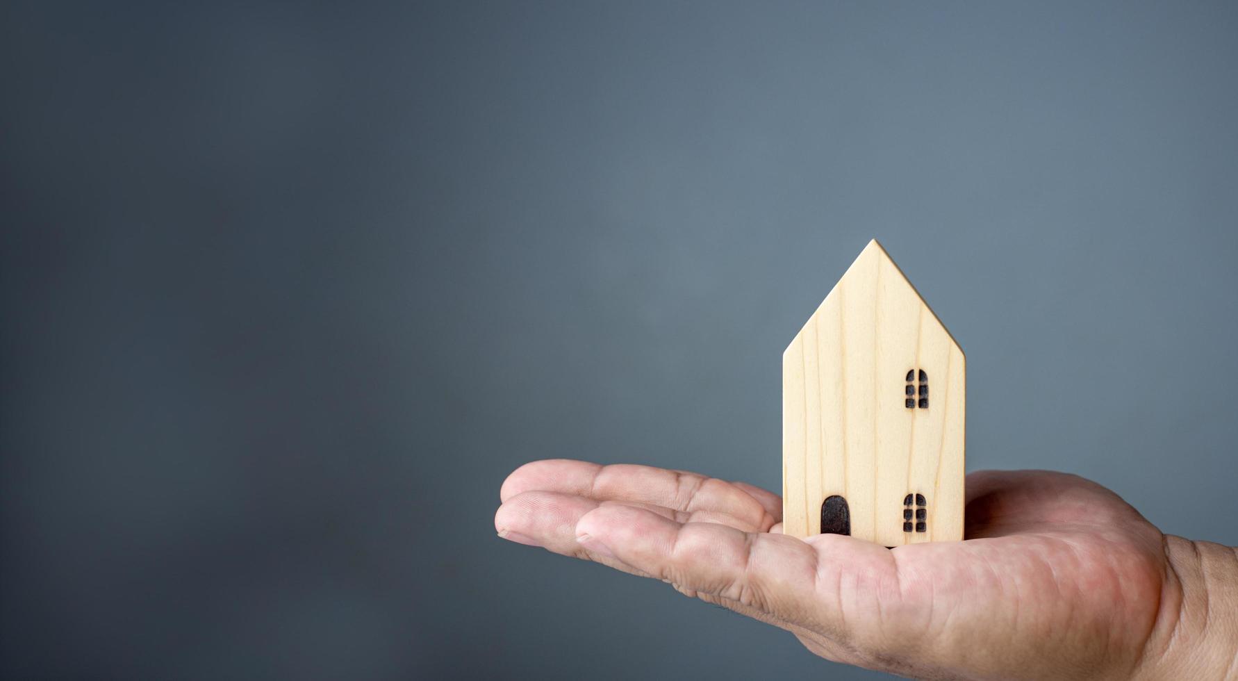 concepto de vender una casa. una mano sostiene una casa modelo sobre un fondo gris. agente de bienes raíces ofrece casa, seguro de propiedad y seguridad, conceptos de vivienda asequible, vendedor. foto