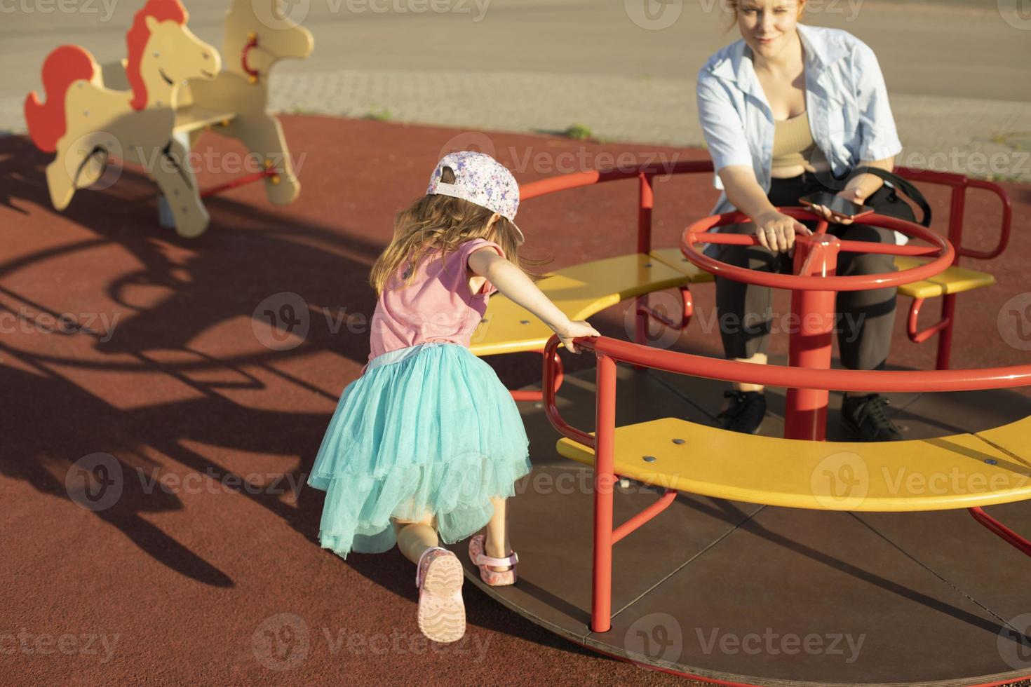 Child on carousel. Kids in playground. Girl spins swing. Details of game in summer. Bright frame game preschoolers. photo
