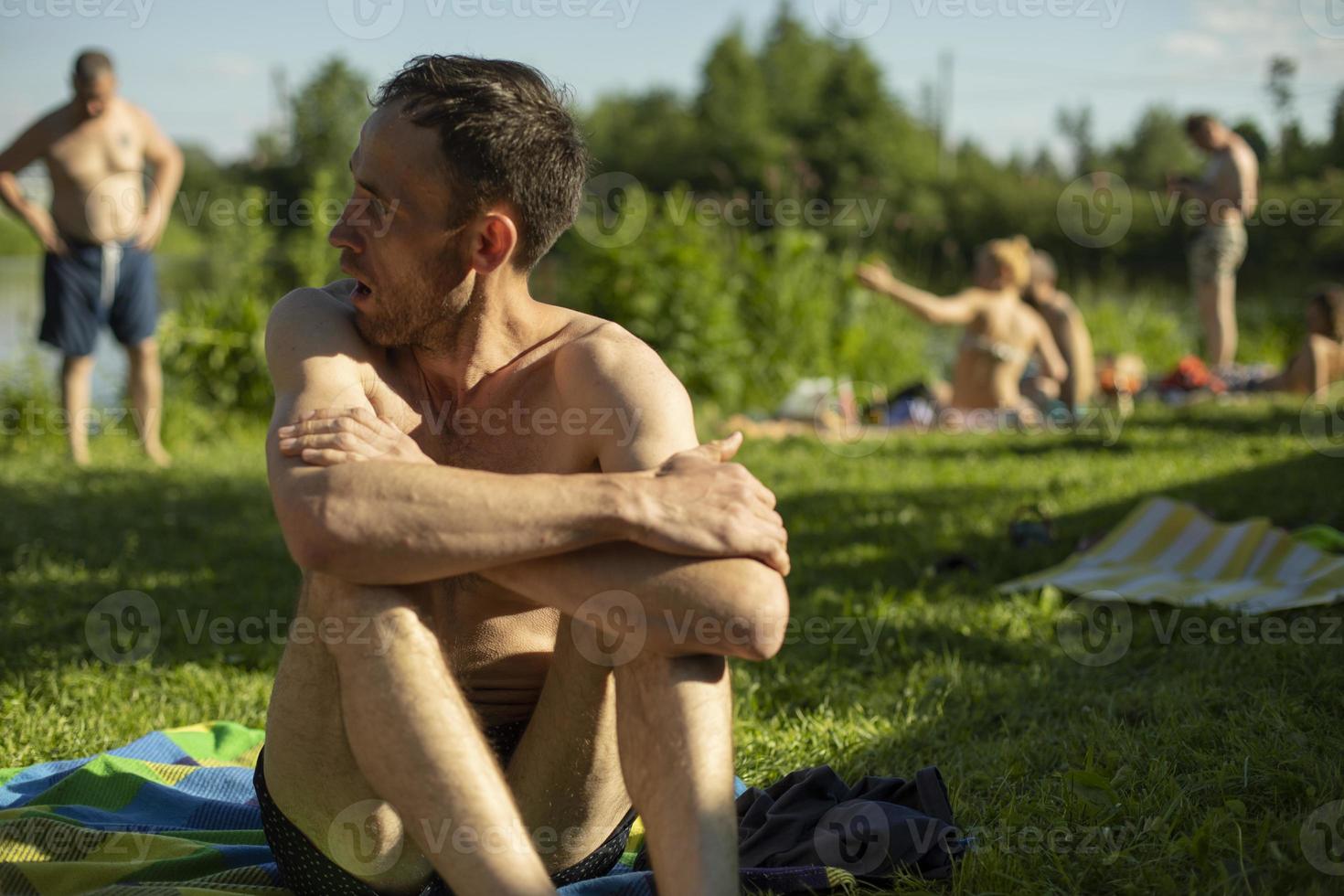 Guy sits on beach in summer. Man sunbathes in sun. Relax on hot day. photo