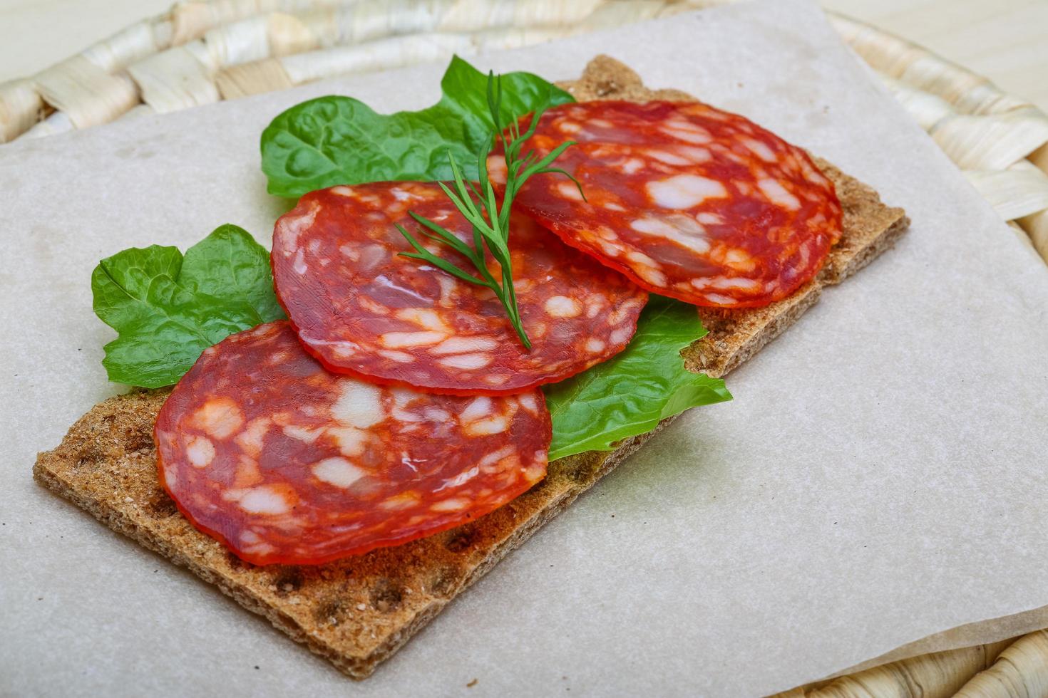 Sándwich de salami sobre tablero de madera y fondo de madera foto