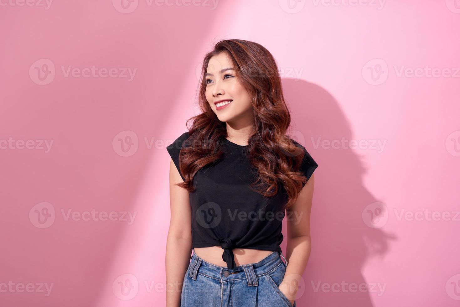 beautiful portrait Asian cheerful young girl poses in casual clothes with beaming smile standing isolated on pink background photo