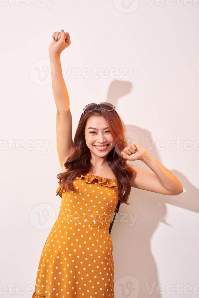 joven y hermosa mujer asiática bailando feliz y alegre, sonriendo en movimiento casual sobre fondo beige foto