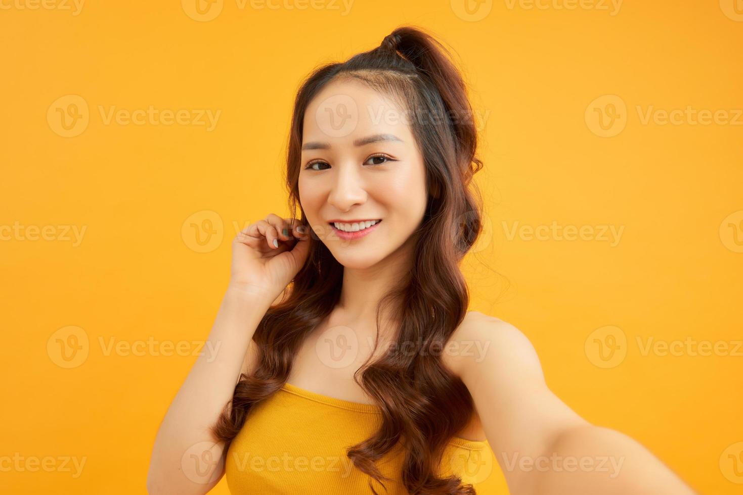 Portrait of cool cheerful girl holding smart phone in hand shooting selfie isolated on orange background enjoying weekend vacation photo