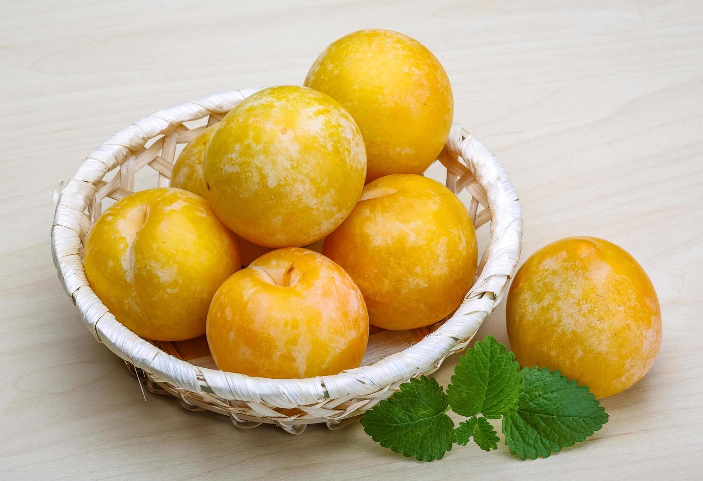 Yellow plums in a basket on wooden background photo