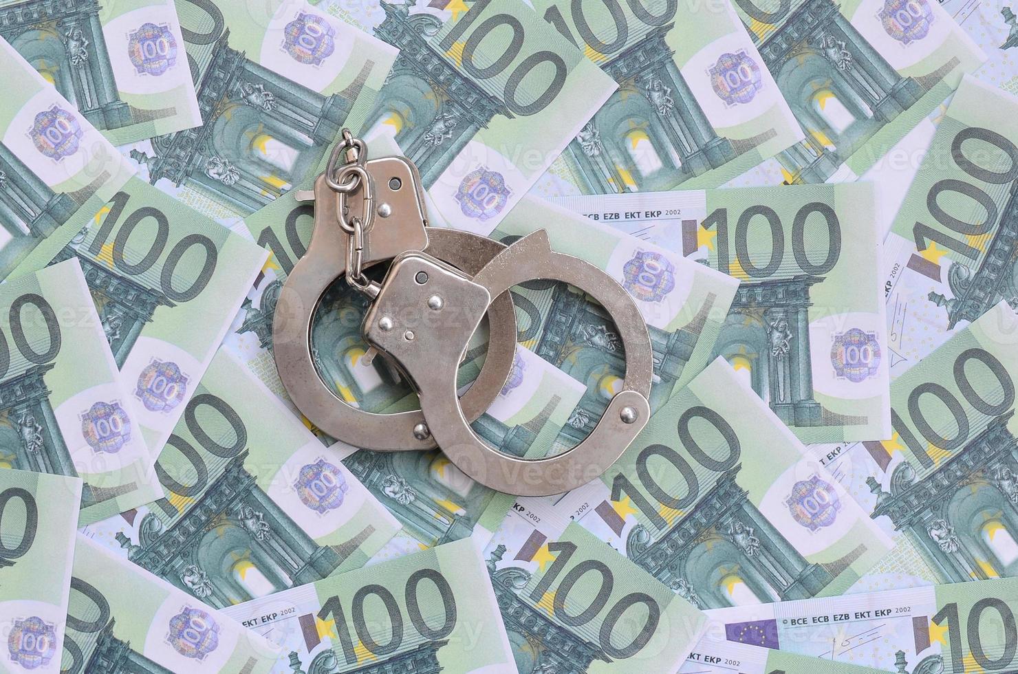 Police handcuffs lies on a set of green monetary denominations of 100 euros. A lot of money forms an infinite heap photo