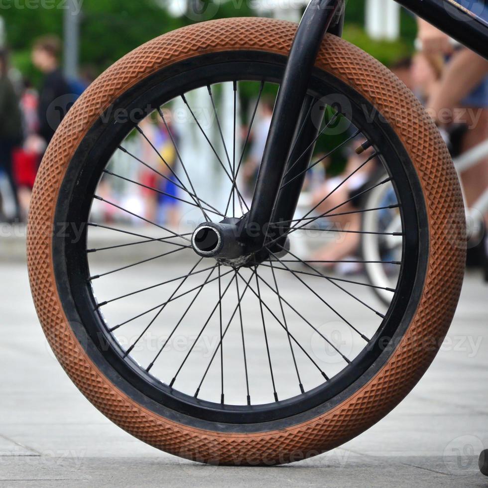 A BMX bike wheel against the backdrop of a blurred street with cycling riders. Extreme Sports Concept photo