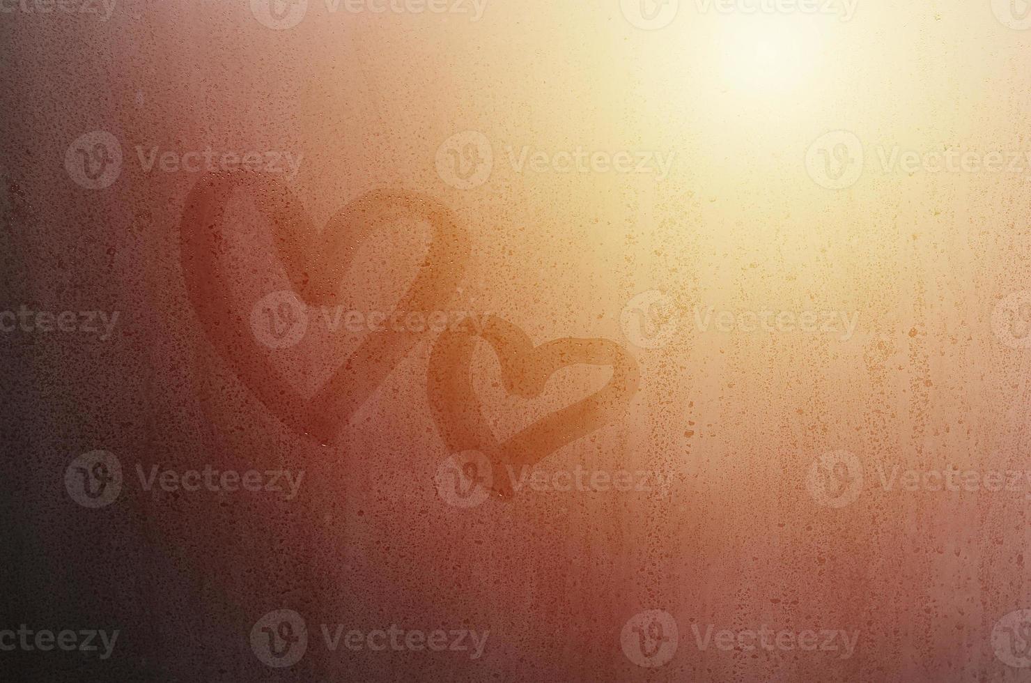 Couple of abstract blurred love heart symbol drawn by hand on the wet window glass with sunlight background. Template for Valentine Day postcards photo