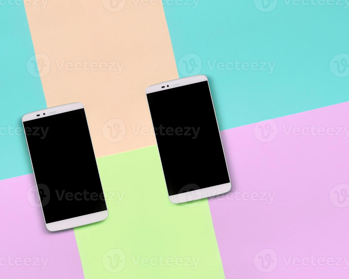 Two modern smartphones with black screens on background of fashion pastel pink, blue, coral and lime colors photo