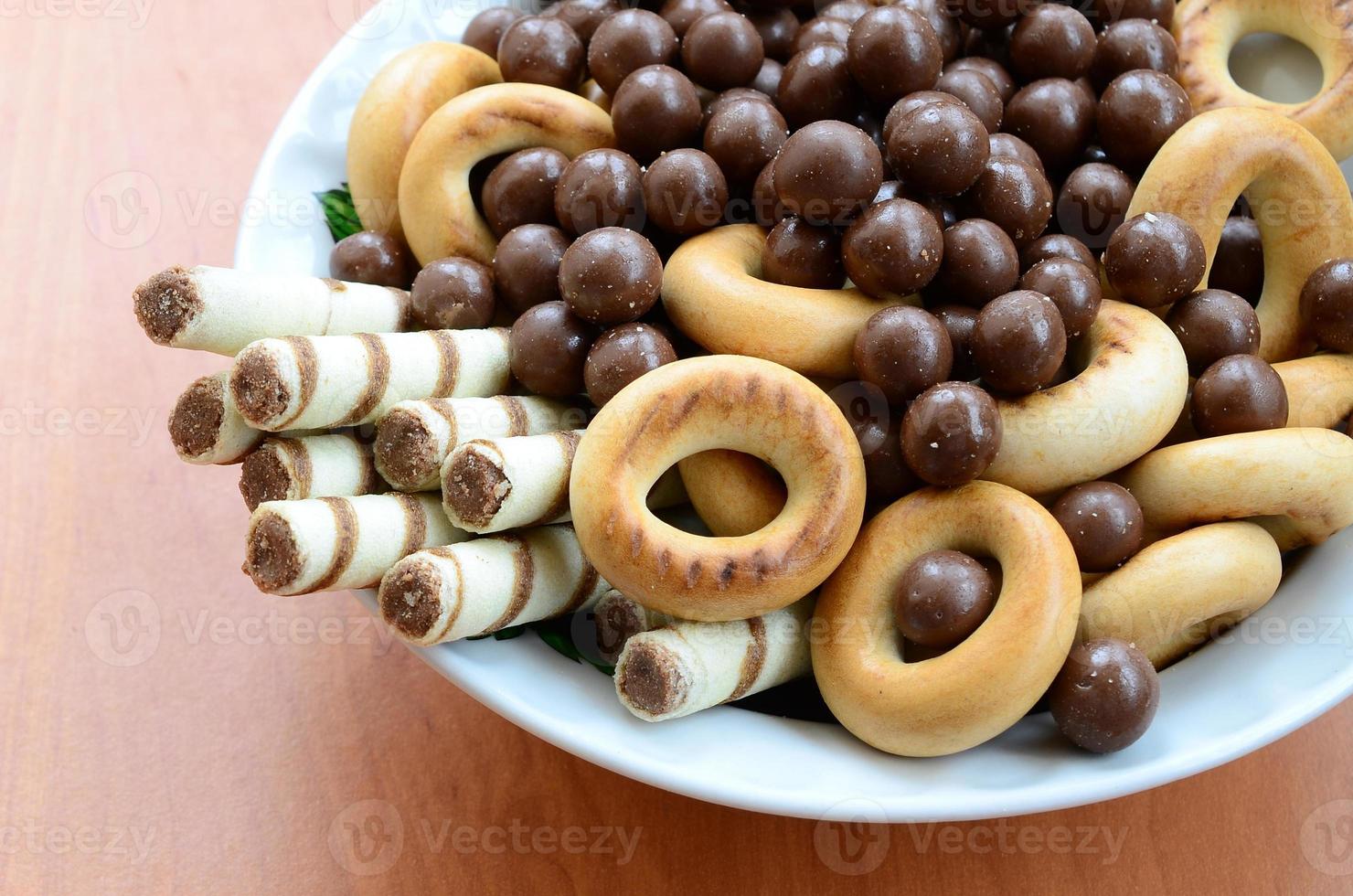 Crispy tubules, chocolate melting balls and bagels lie in a white plate on a wooden table. Mix of various sweets photo