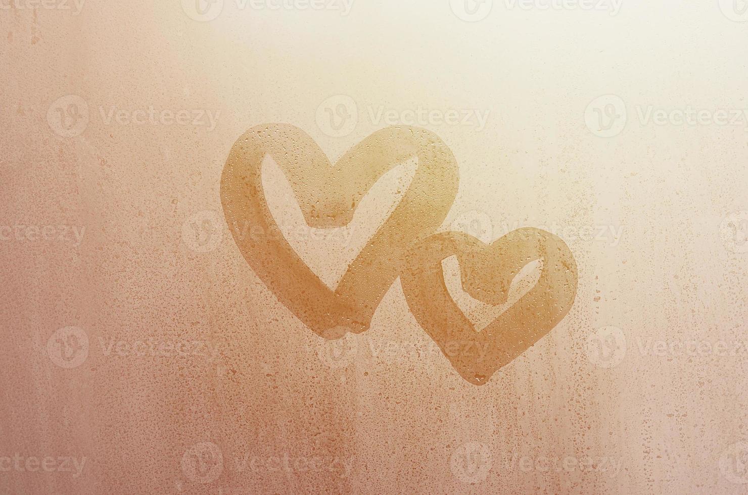 Couple of abstract blurred love heart symbol drawn by hand on the wet window glass with sunlight background. Template for Valentine Day postcards photo