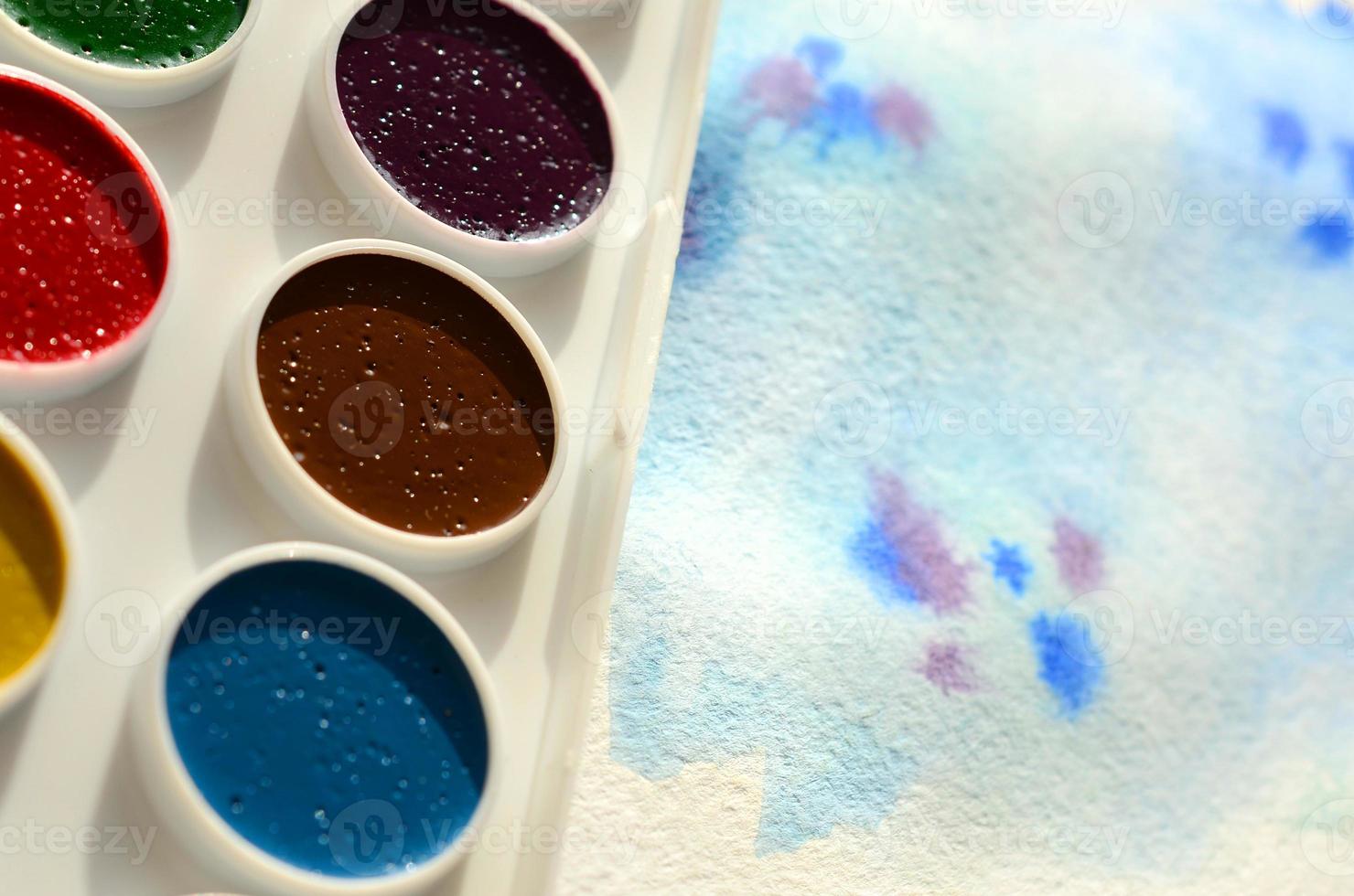 A new set of watercolors lies on a sheet of paper, which shows an abstract watercolor drawing in the form of blue strokes. The concept of amateur painting among teenagers photo