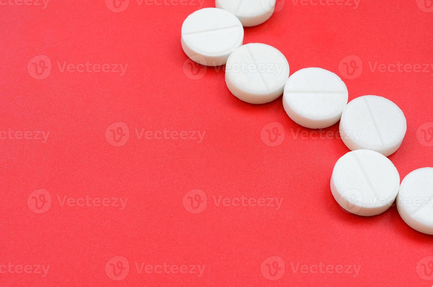 A few white tablets lie on a bright red background surface. Background image on medical and pharmaceutical topics photo
