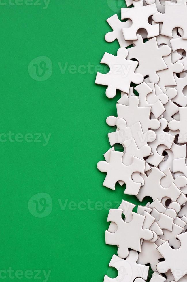 A pile of uncombed elements of a white jigsaw puzzle lies on the background of a green surface. Texture photo with copy space for text
