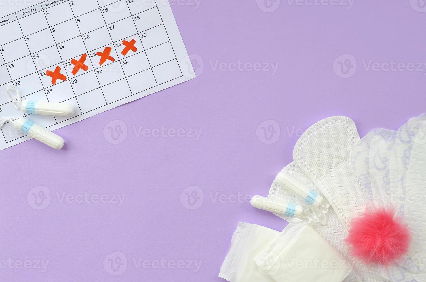 Menstrual pads and tampons on menstruation period calendar flat lay on lilac background photo