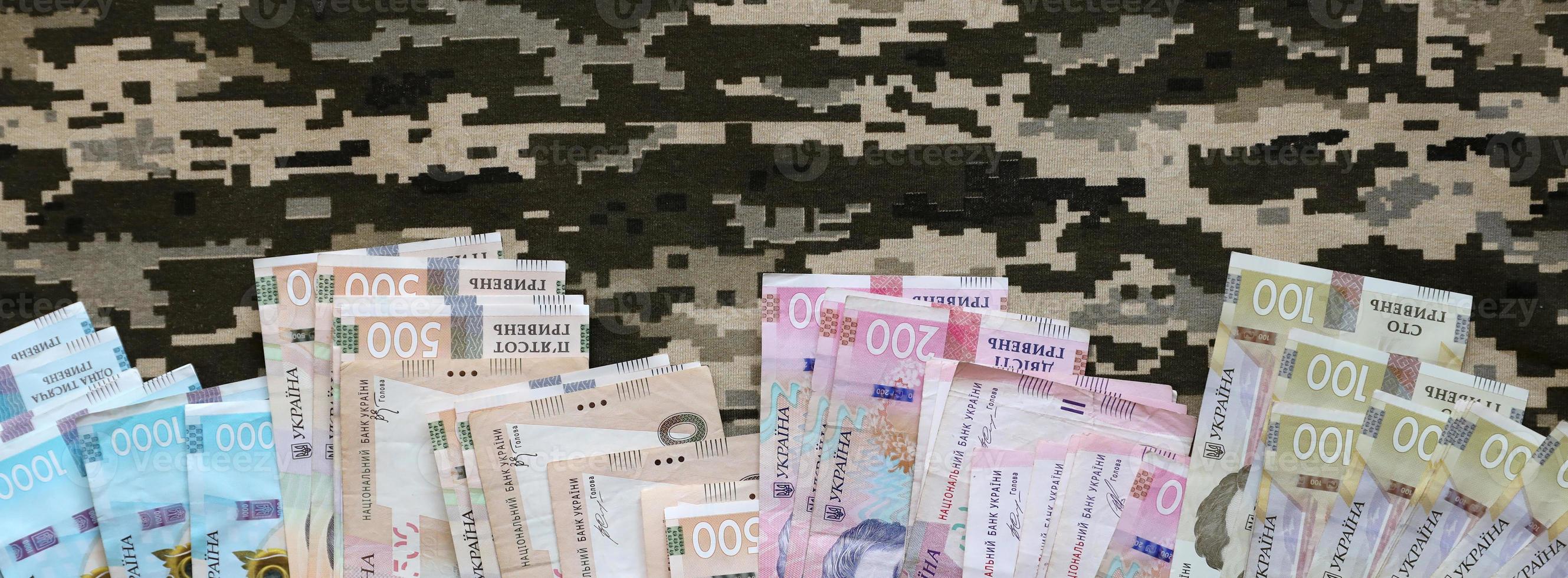 Ukrainian hryvnya bills on fabric with texture of Ukrainian military pixeled camouflage. Cloth with camo pattern in grey, brown and green pixel shapes photo
