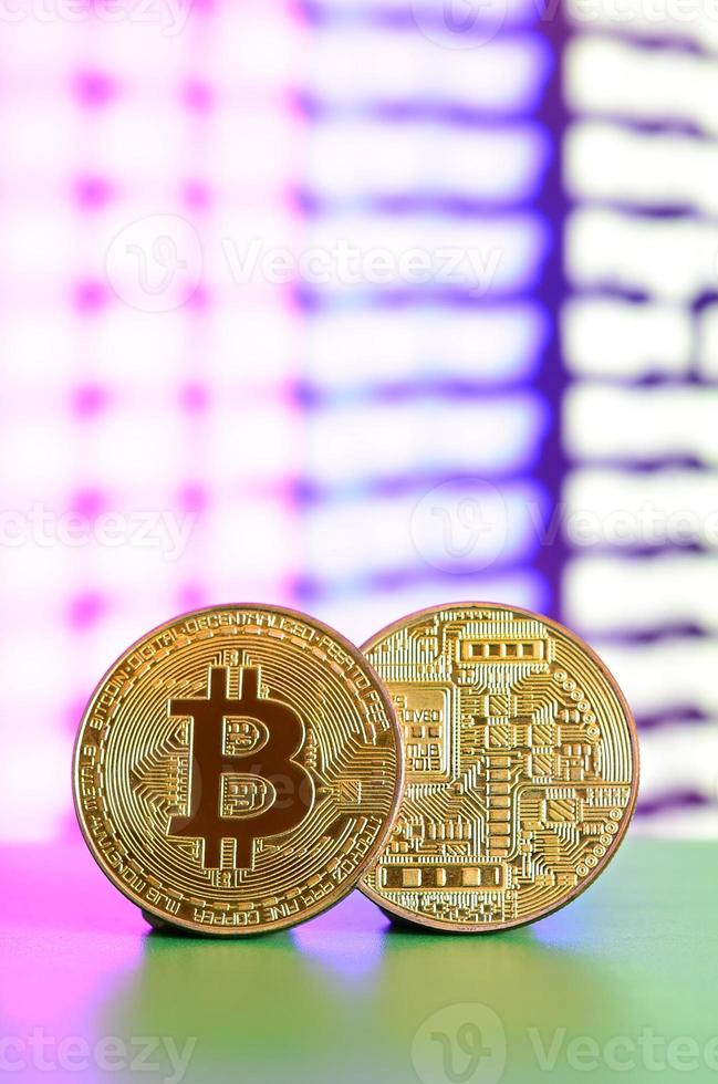 Two gold bitcoins lie on the green surface on the background of the display, which shows the process of mining the crypto currency photo