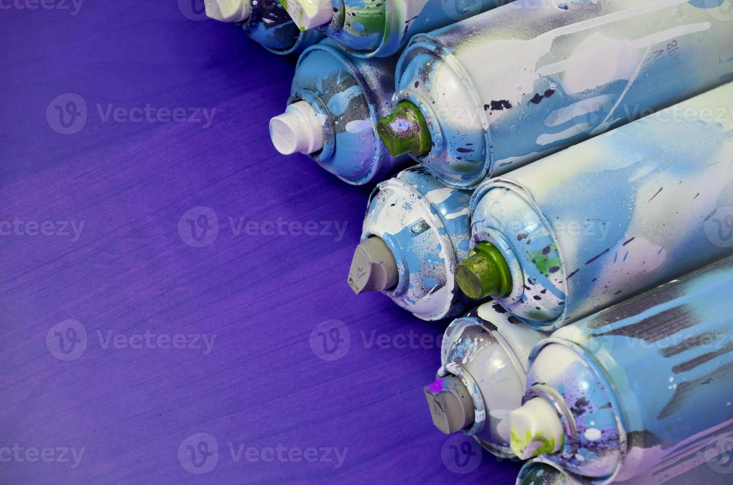 Still life with a large number of used colorful spray cans of aerosol paint lying on the treated wooden surface in the artist's graffiti workshop. Dirty and stained cans for spray art photo