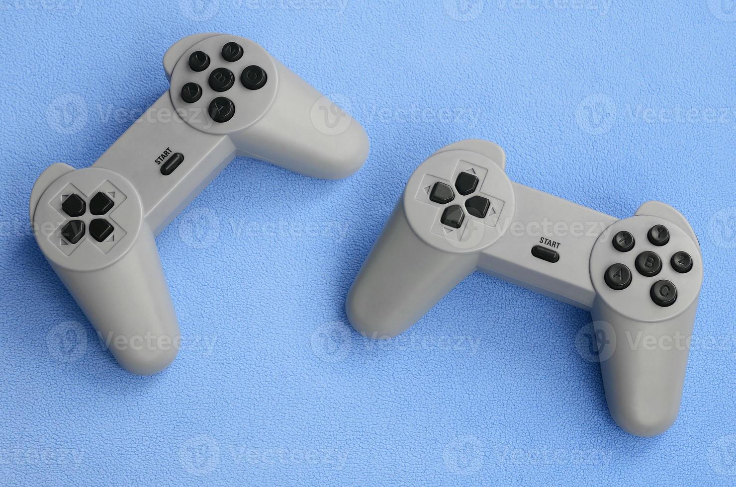 concepto de juegos. dos joysticks de almohadilla se encuentran sobre la manta de tela de lana azul peluda. controladores para videojuegos en una textura de fondo de material de felpa suave azul claro foto