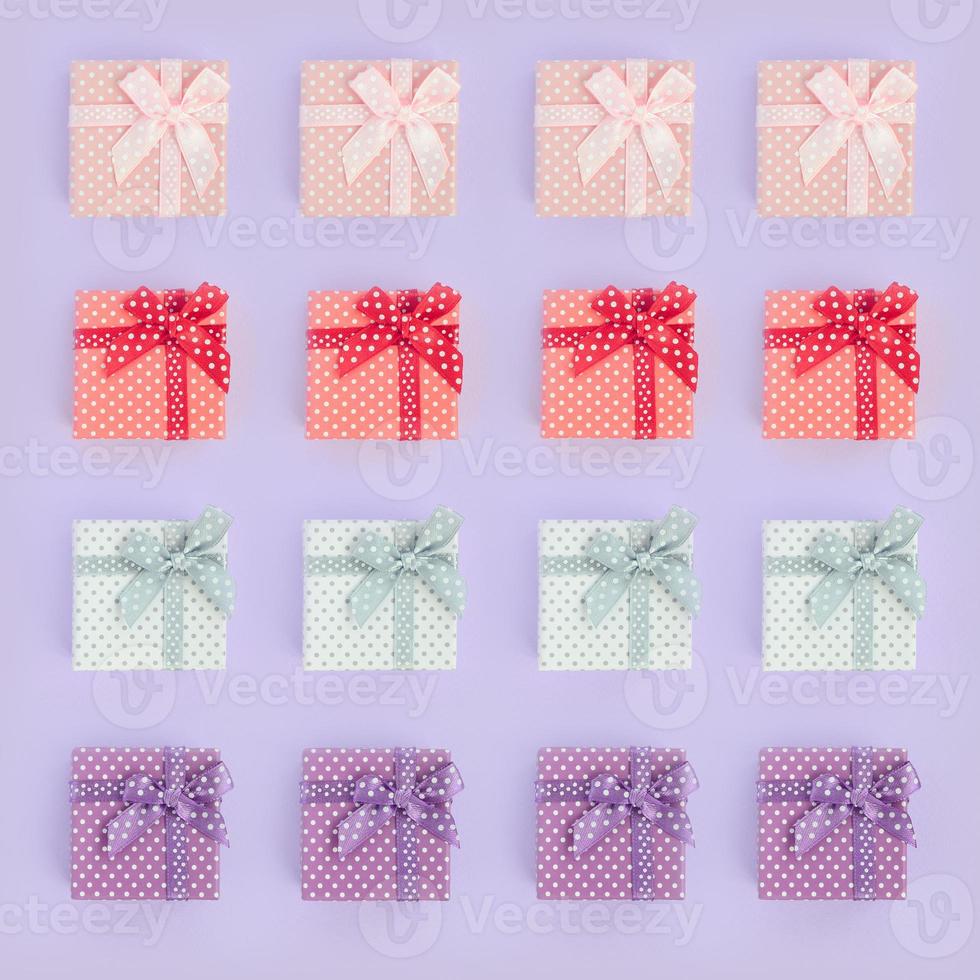 Piles of a small colored gift boxes with ribbons lies on a violet background. Minimalism flat lay top view pattern photo