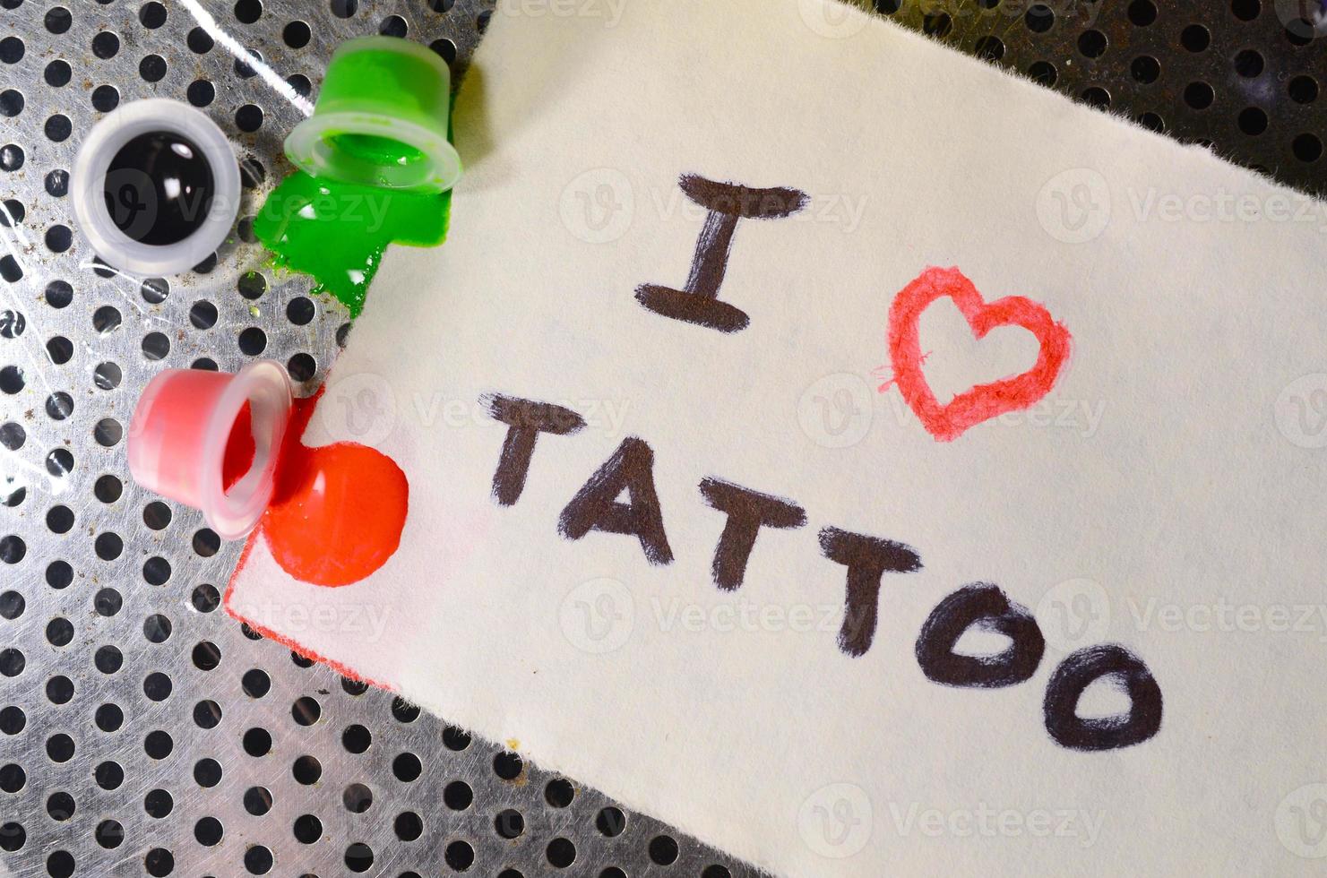 me encanta el tatuaje el texto está escrito en una pequeña hoja de papel junto a las tapas volcadas con tinta de tatuaje de color foto