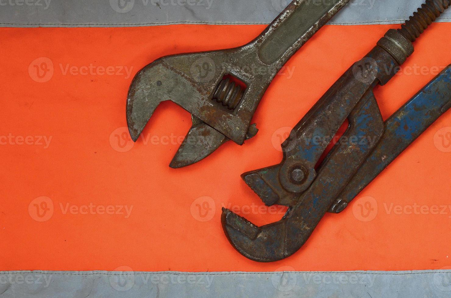 Adjustable and pipe wrenches against the background of an orange signal worker shirt photo