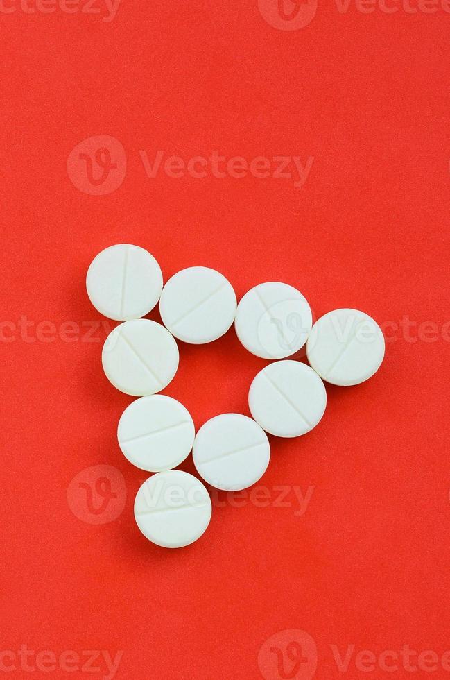 Several white tablets lie on a bright red background in the form of an even triangle. Background image on medicine and pharmaceutical topics photo