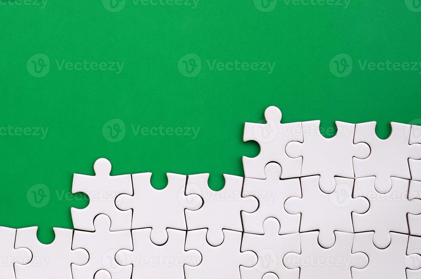 Fragment of a folded white jigsaw puzzle on the background of a green plastic surface. Texture photo with copy space for text