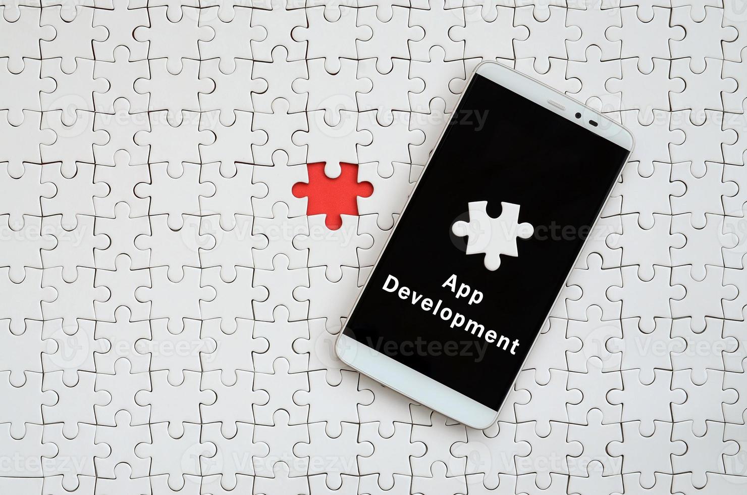 A modern big smartphone with a touch screen lies on a white jigsaw puzzle in an assembled state with inscription. App development photo